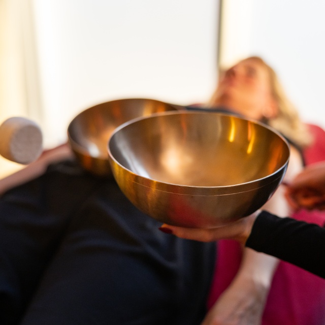 Klangschale und eine Frau, die im Hintergrund auf der Massageliege entspannt