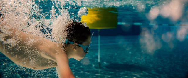 Ein Kind mit Schwimmbrille ist tauchen in einem Freibadbecken zu sehen.